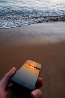 A serene beach scene with a traveler using a smartphone to check their funded trip status on Viamente.