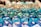 A collection of colorful, multi-sided gaming dice with numbers, predominantly in shades of blue and green, arranged closely and reflecting light.