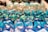 A collection of colorful, multi-sided gaming dice with numbers, predominantly in shades of blue and green, arranged closely and reflecting light.