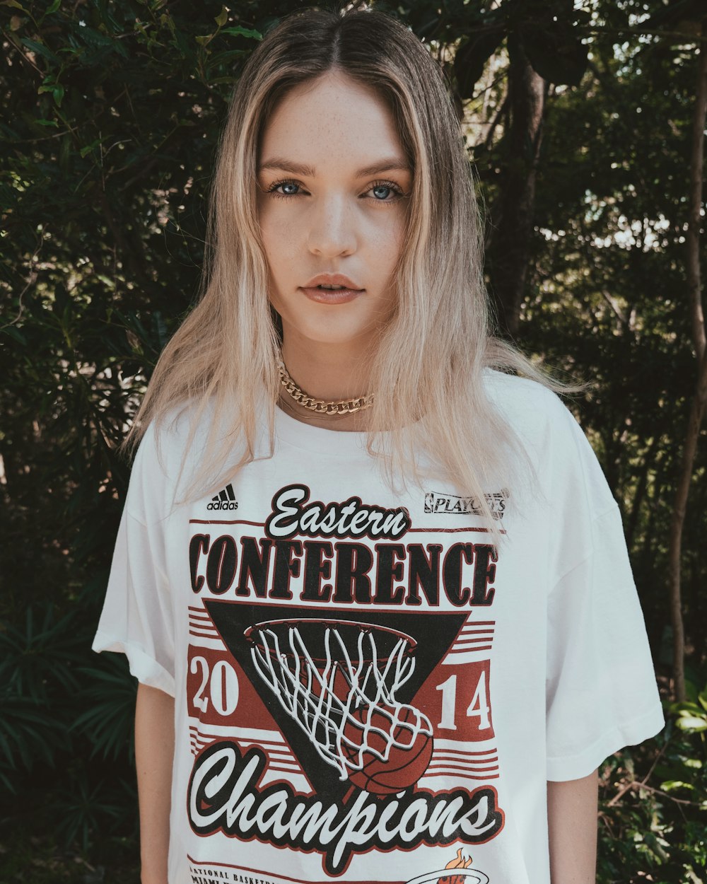 woman in white crew neck t-shirt standing near green tree during daytime