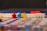 Colorful board game pieces are arranged on a game board. Three key pieces, shaped like small figures, are positioned prominently in red, blue, and yellow. In the background, a white structure reminiscent of a wall or castle adds an element of architecture to the scene. The game board is partially visible, showing a mosaic of colors and patterns.