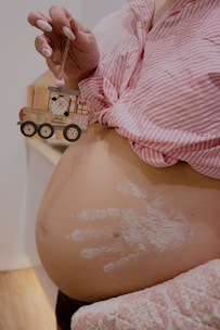 a pregnant woman holding a toy car on her belly