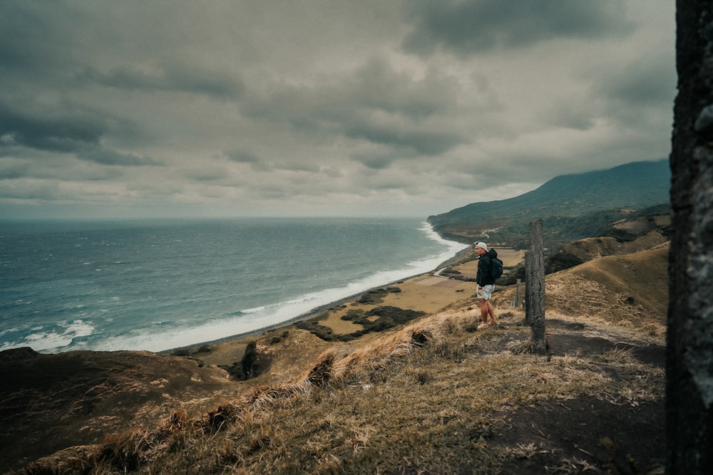 people standing on brown rock formation near sea under gray clouds during daytime