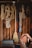 A collection of various ropes are neatly hung on hooks against a wooden wall in a workshop or garage. A long-handled broom is positioned in the center. The ropes vary in thickness and color, including beige, blue, and red. A few other tools and accessories are partially visible, such as a toolbox.