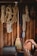 A collection of various ropes are neatly hung on hooks against a wooden wall in a workshop or garage. A long-handled broom is positioned in the center. The ropes vary in thickness and color, including beige, blue, and red. A few other tools and accessories are partially visible, such as a toolbox.