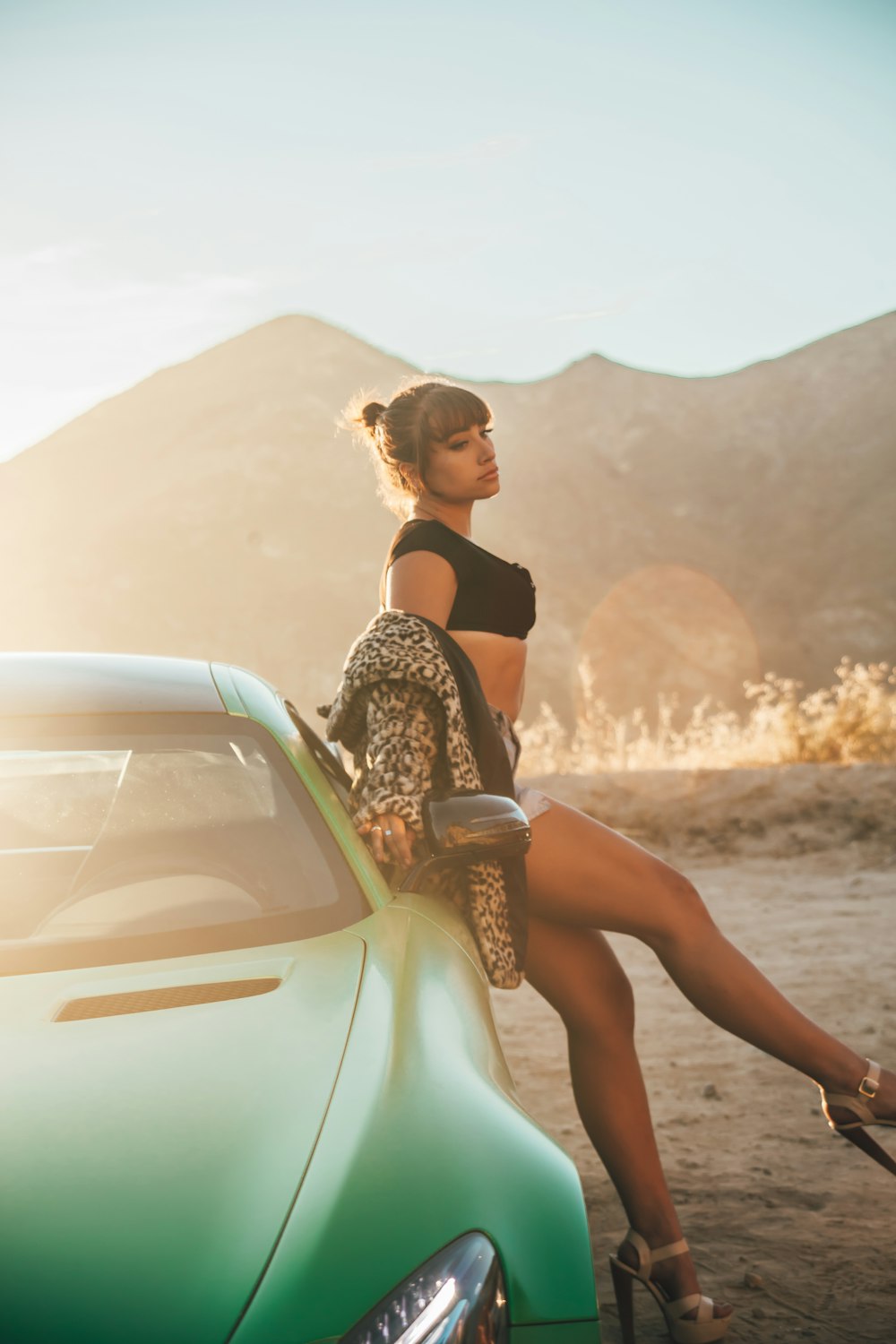 woman in black tank top and teal skirt leaning on white car
