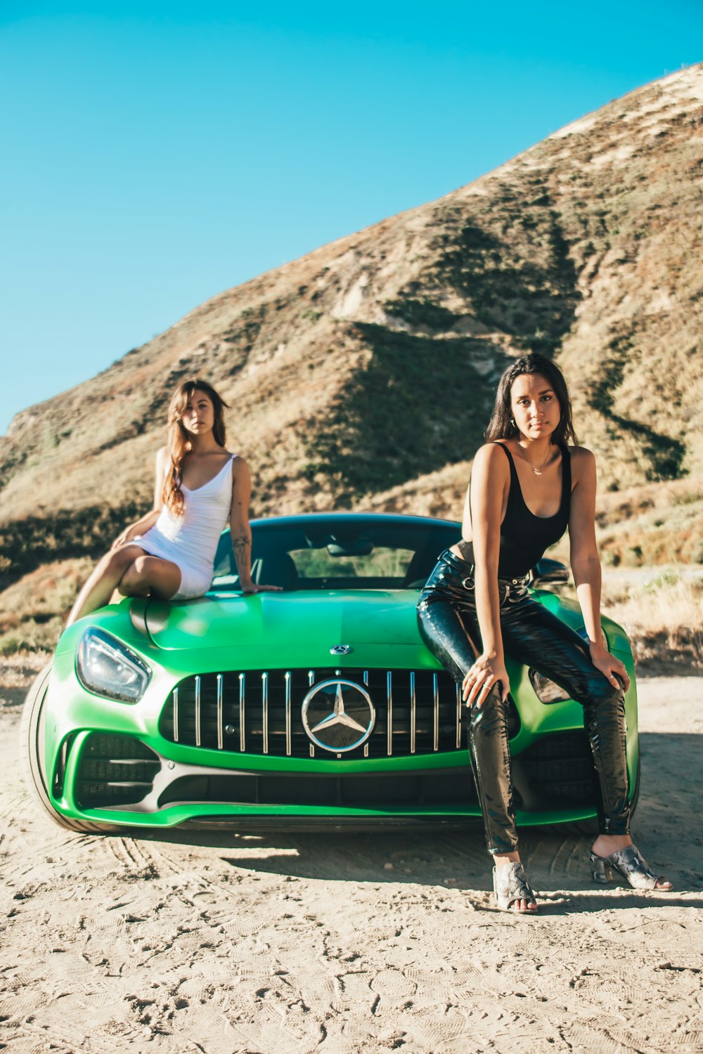 woman in black tank top and black pants leaning on green car