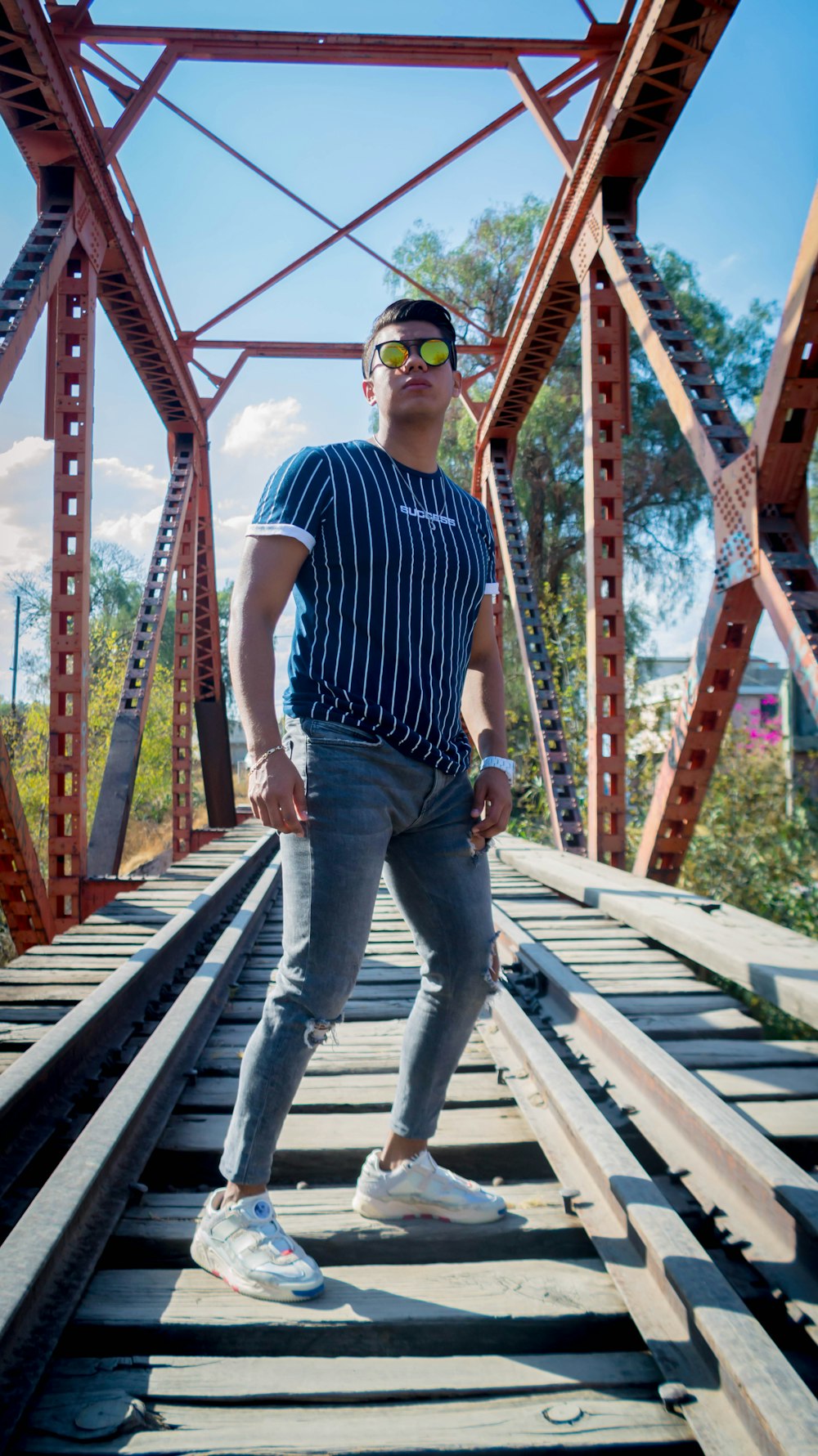 man in blue and white stripe polo shirt and blue denim jeans standing on brown wooden