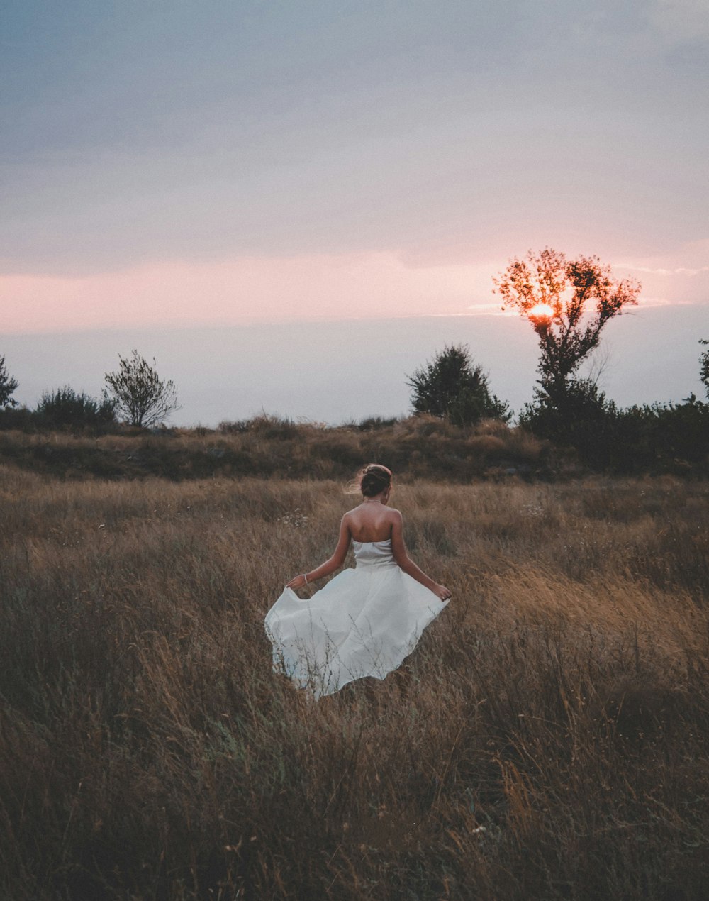 夕暮れ時の緑の芝生の上に立つ白いドレスを着た女性