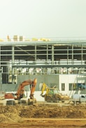 yellow excavator near white and blue building during daytime