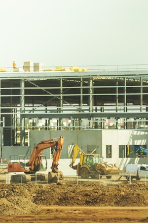 A yellow excavator working beside a white and blue school building during a construction project