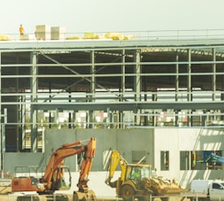 yellow excavator near white and blue building during daytime