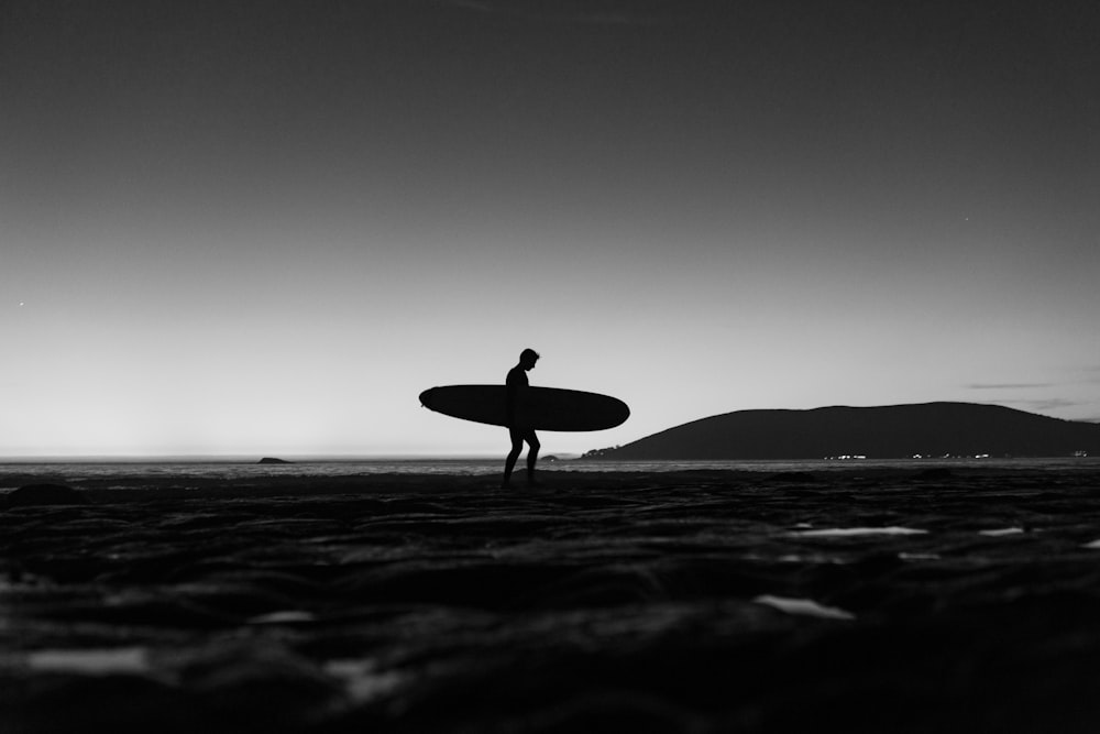 silhouette di uomo che tiene la tavola da surf che cammina sulla spiaggia