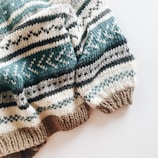 A cozy knitted sweater with a pattern of horizontal stripes in various colors. The texture is thick and the design includes alternating colors with geometric motifs.