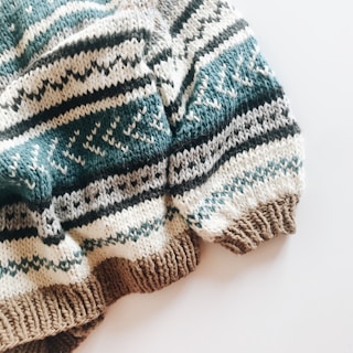 A cozy knitted sweater with a pattern of horizontal stripes in various colors. The texture is thick and the design includes alternating colors with geometric motifs.