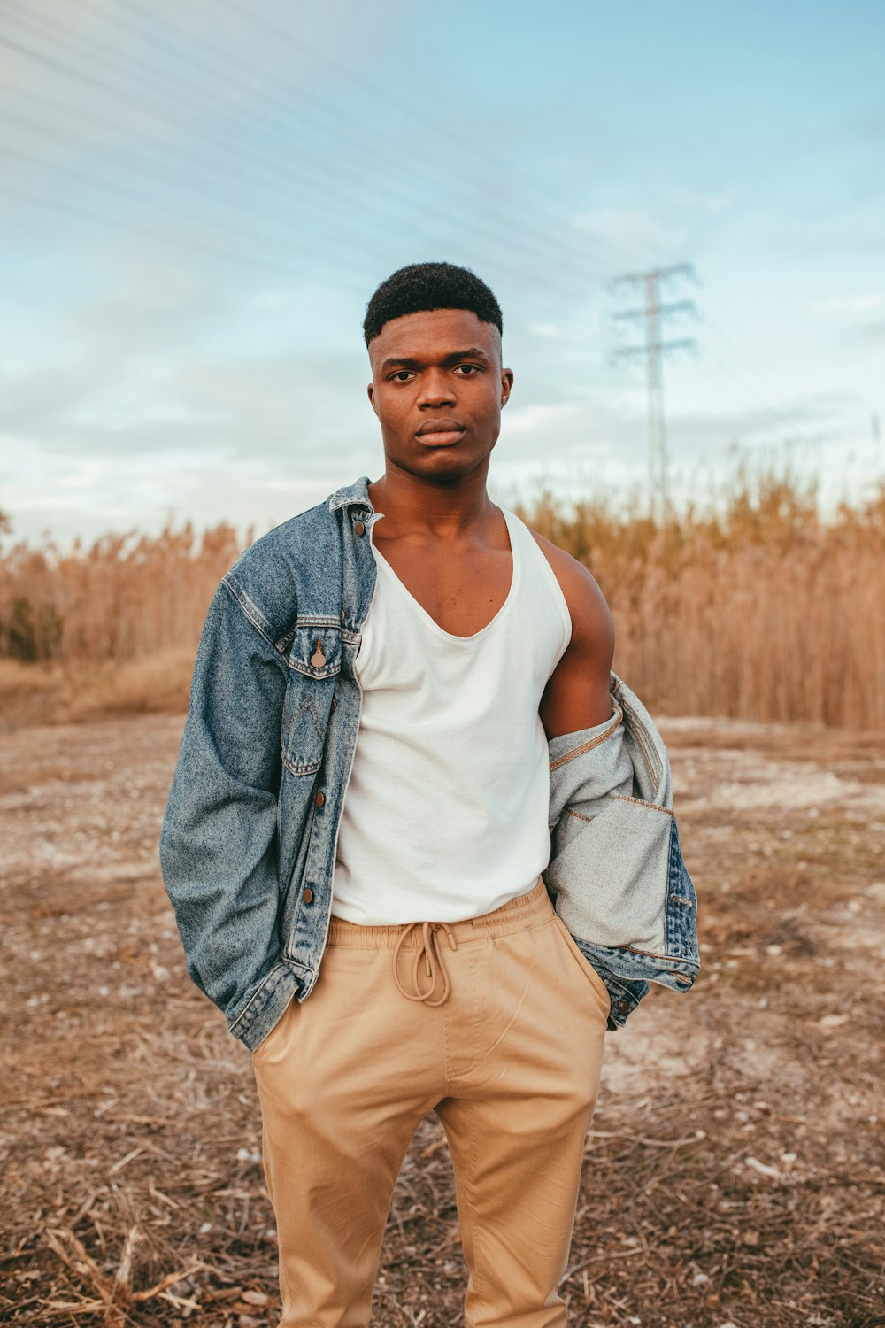 man in white tank top and blue denim jacket standing on brown field during daytime