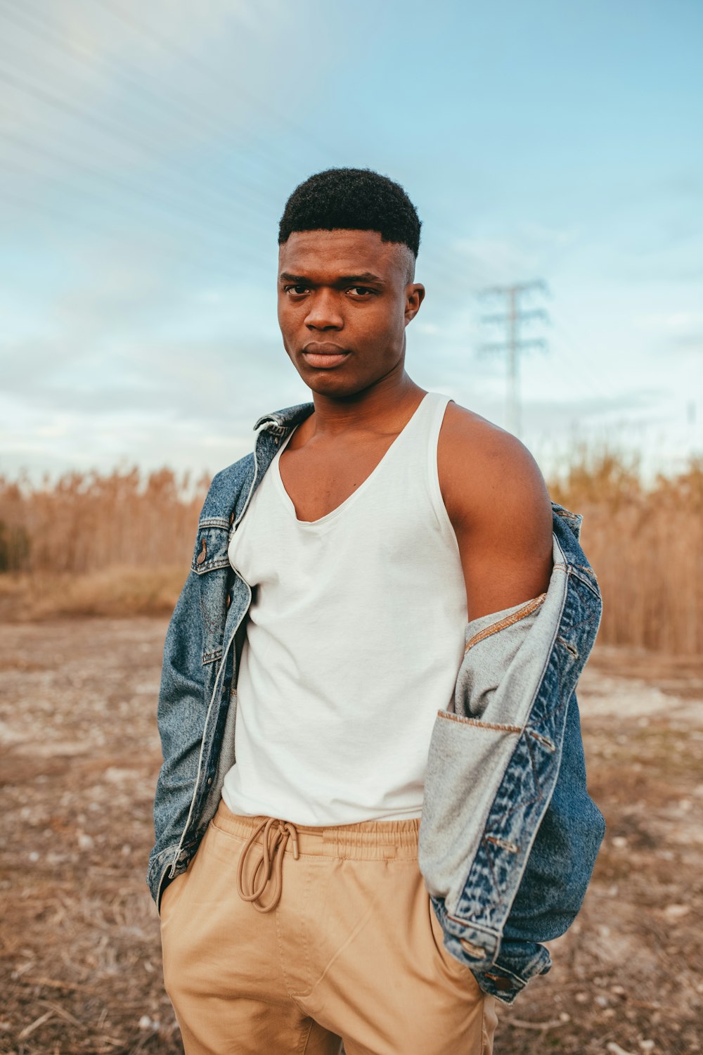 man in white tank top and blue denim jacket standing on brown field during daytime