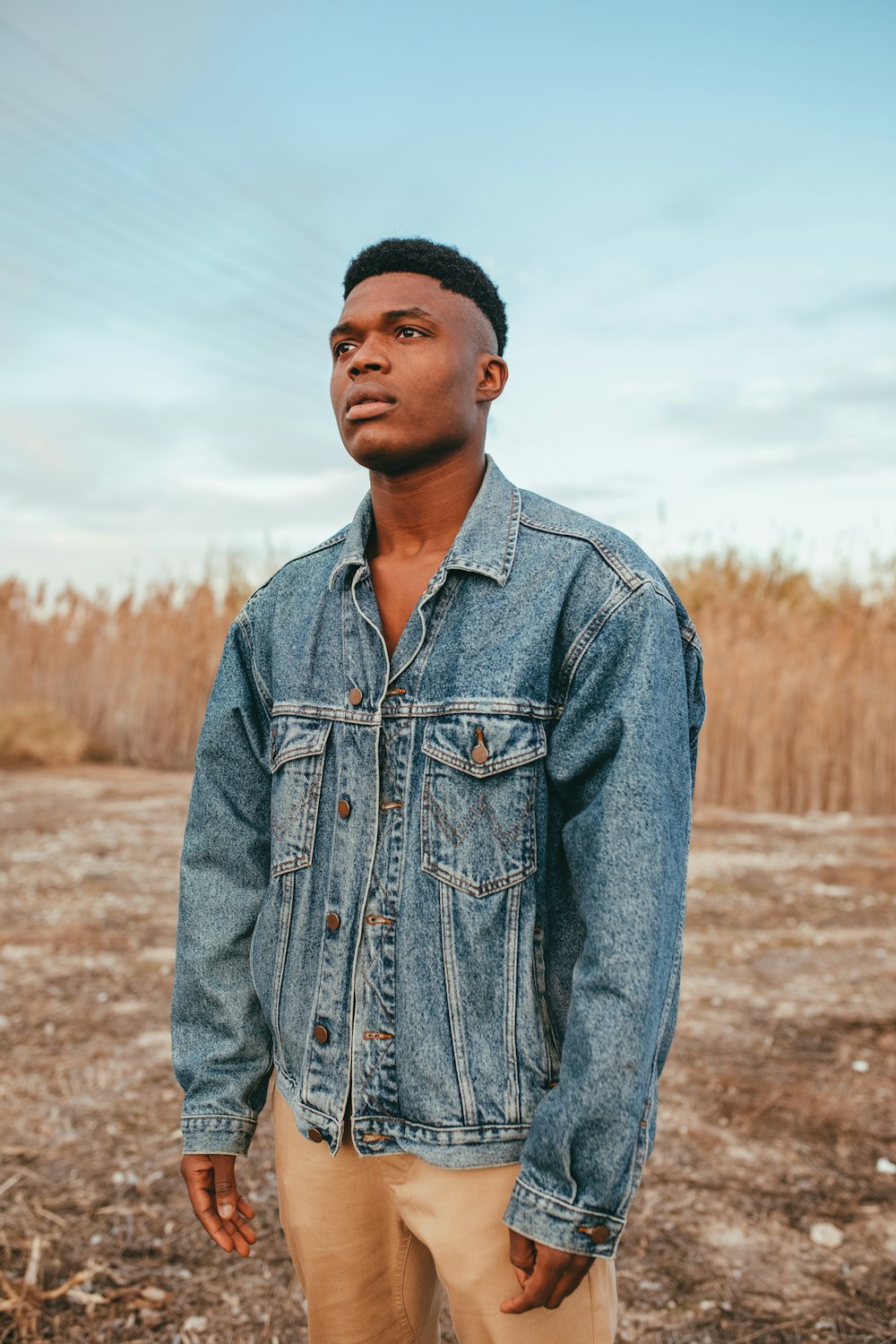 man in blue denim jacket standing on brown field during daytime