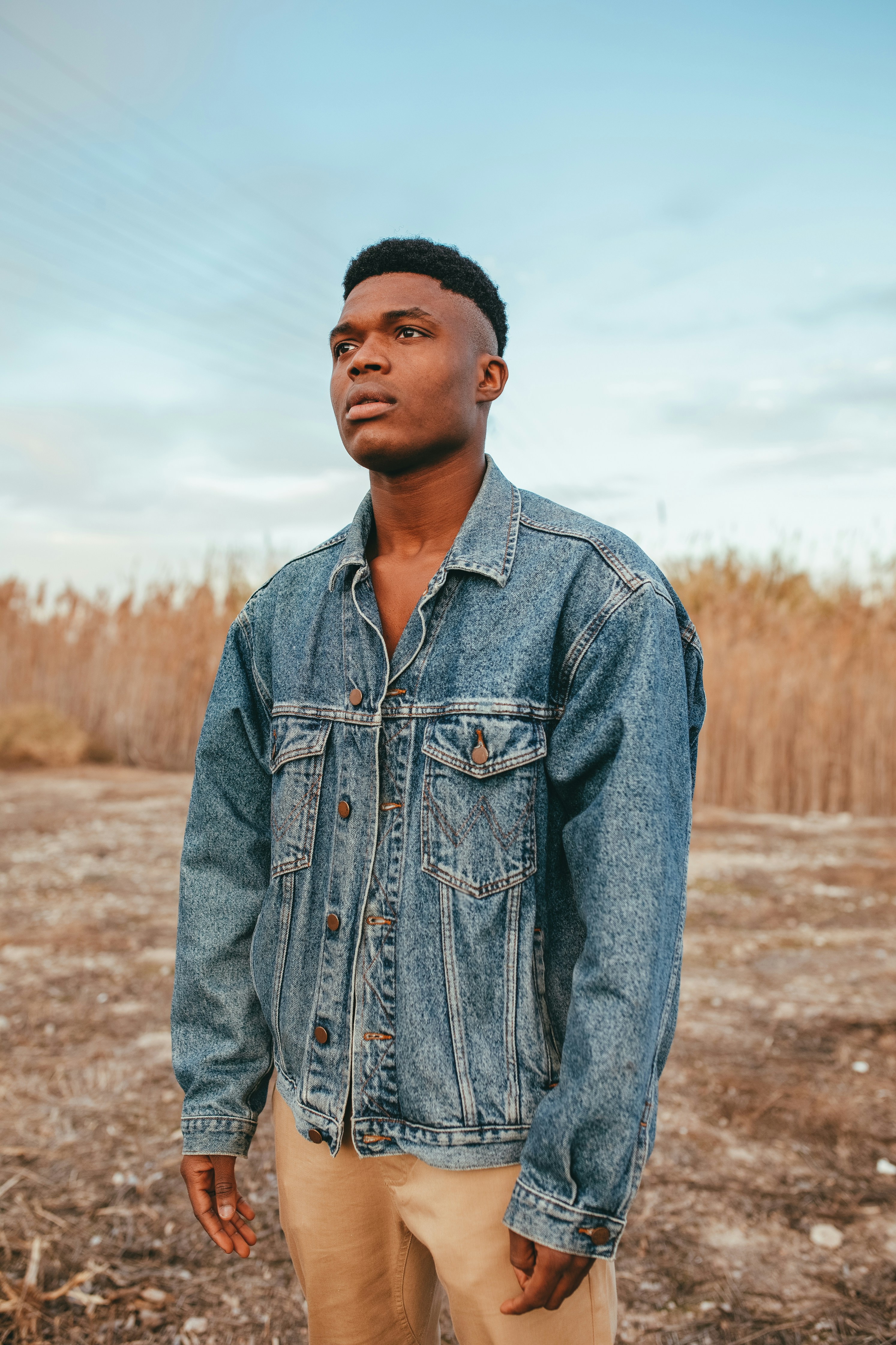 man in blue denim jacket standing on brown field during daytime