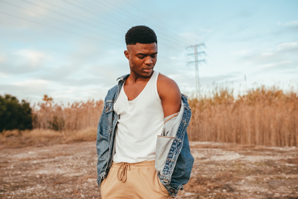 man in white tank top and brown pants standing on brown field during daytime