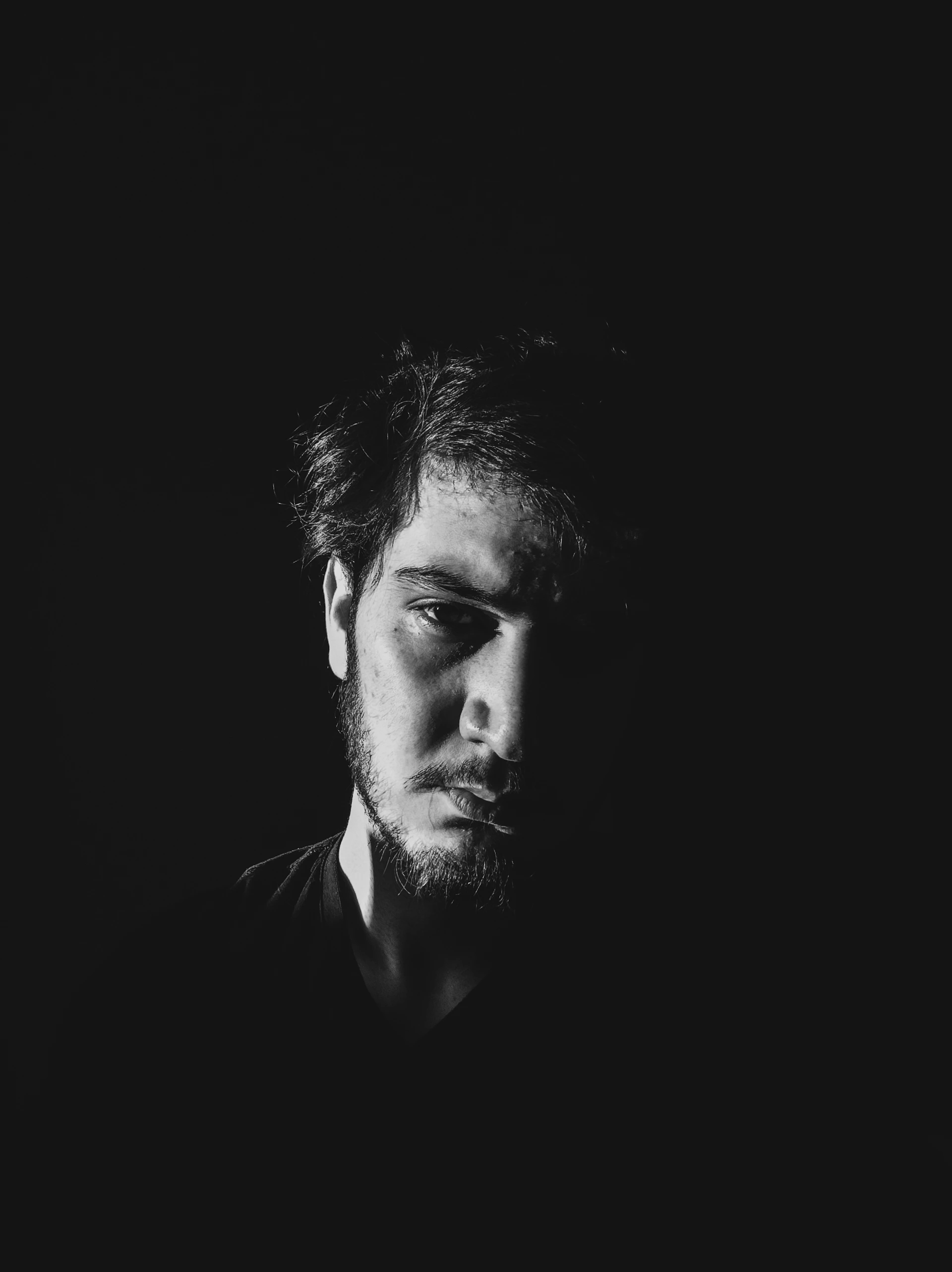 A minimalist portrait featuring sharp contrasts of light and shadow, emphasizing the subject's expression.