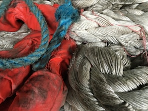 A close-up view of intertwined thick gray ropes and blue and red ropes, with dirt and wear visible on the material.