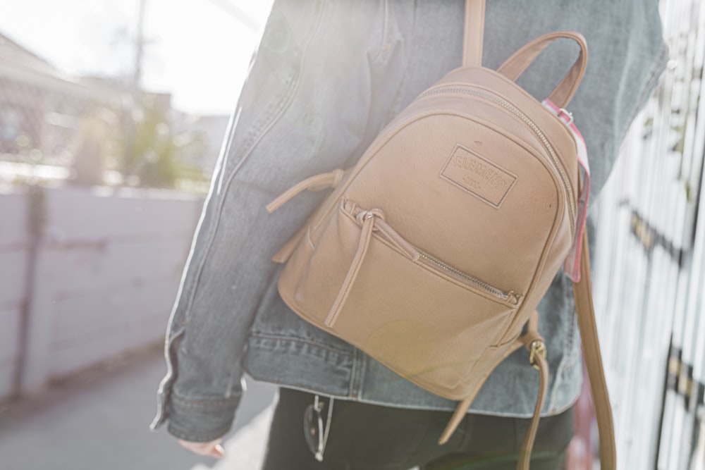 person in blue denim jeans carrying brown leather backpack