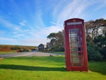 red telephone booth on green grass field under blue sky during daytime
