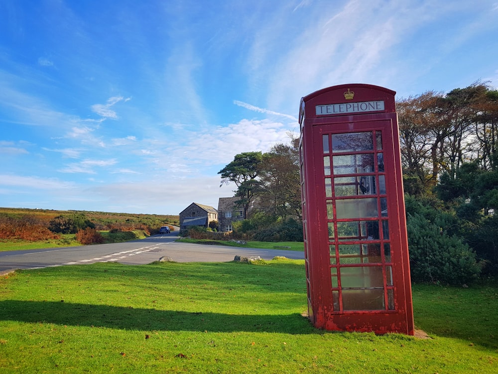 cabina telefónica roja en el campo de hierba verde bajo el cielo azul durante el día