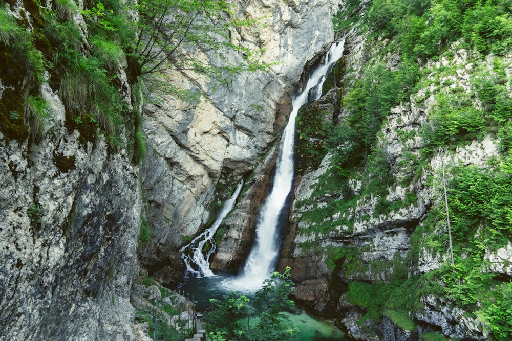 water falls between gray rocky mountain during daytime