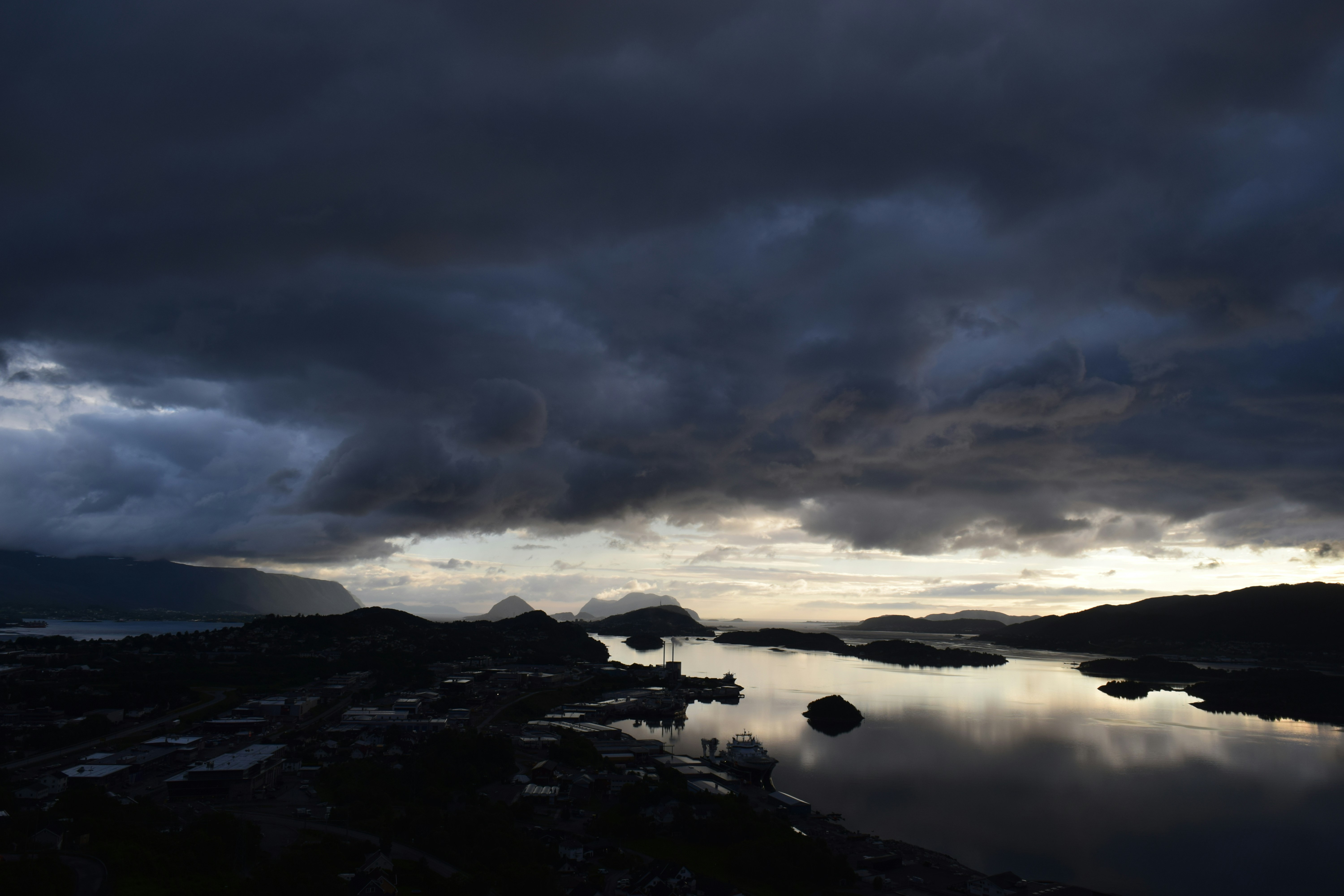 Storm clouds gathering over coastal New England town, dramatic dark sky, calm water before storm