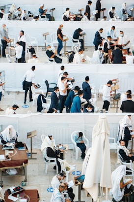 A gathering of people, mostly men, wearing traditional religious garments and masks are engaged in prayer and reading, in an outdoor setting with white plastic chairs and tables. Some individuals are seated, while others are standing, showing diverse activities including reading from religious texts and personal reflection.