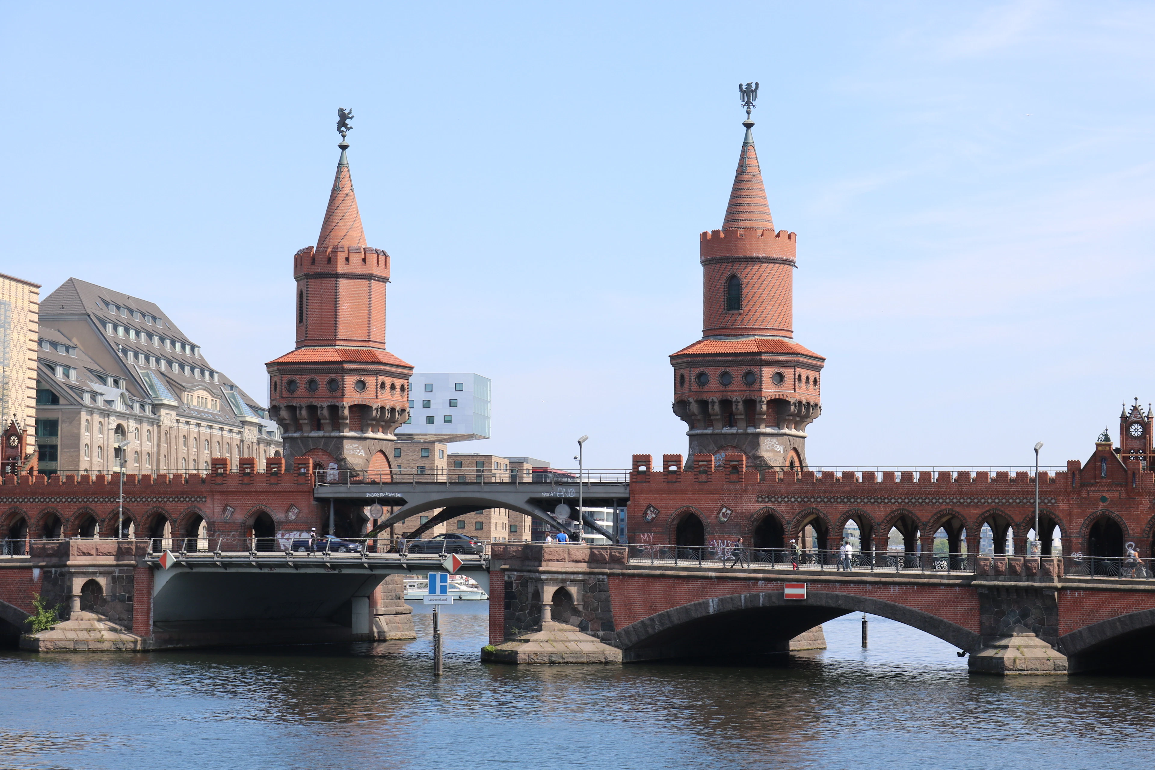 Berlin's red-brick Oberbaum Bridge spans the Spree river under a clear blue sky as a boat passes beneath.
