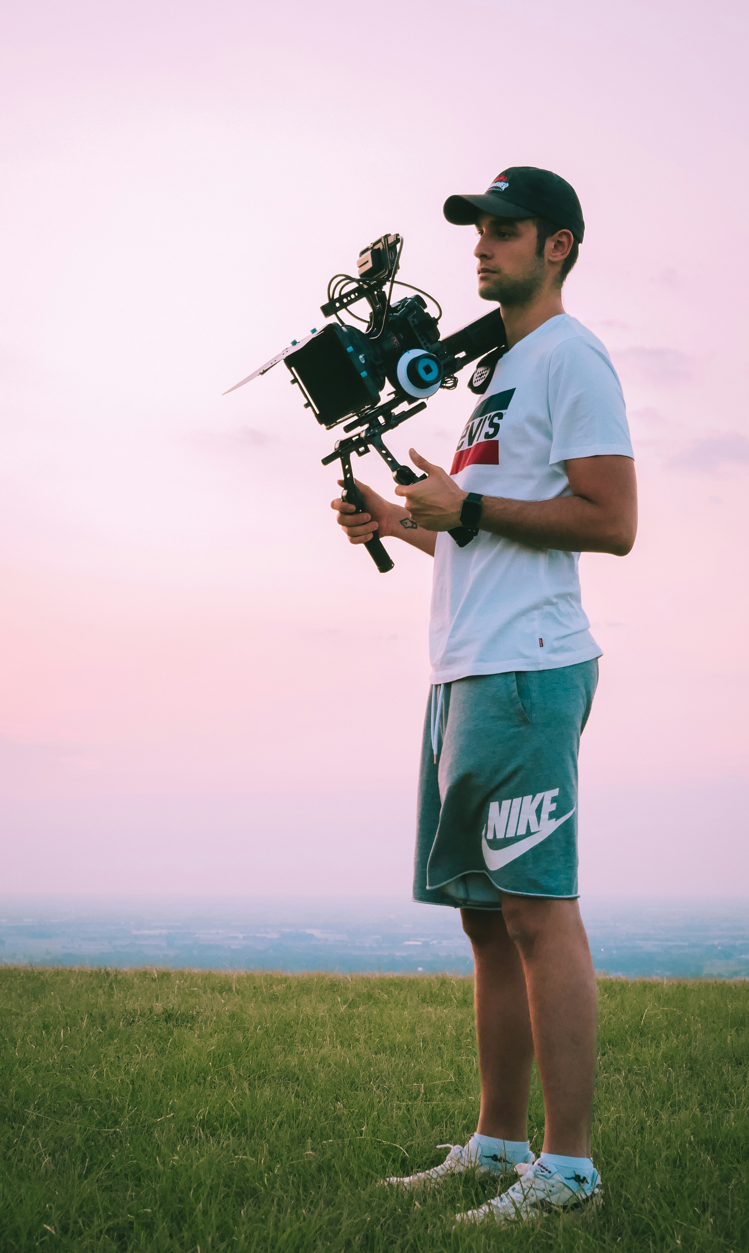 Pria berkaos putih dan celana pendek biru memegang kamera DSLR hitam