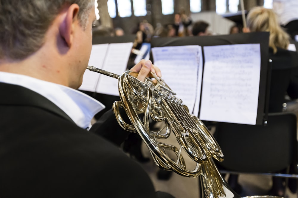 person in black suit jacket playing brass trumpet