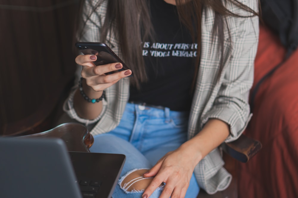 woman in white cardigan holding black smartphone