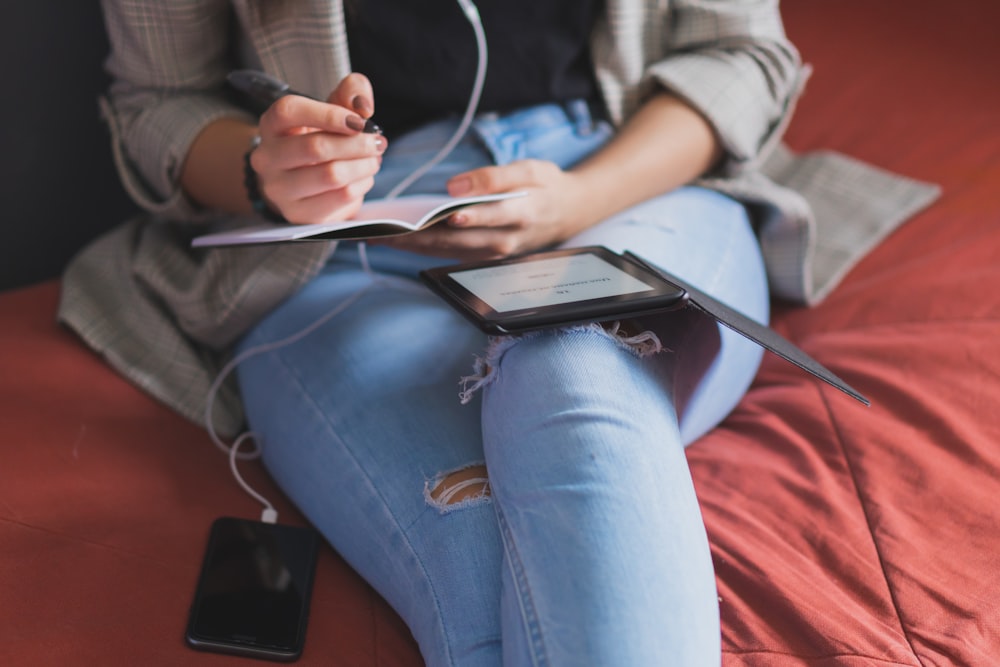 person in blue denim jeans holding white tablet computer