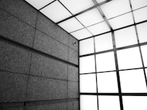 An architectural interior featuring a modern, industrial design with large stone or concrete panels on the walls. The ceiling consists of a grid of square lights, casting a diffused glow.