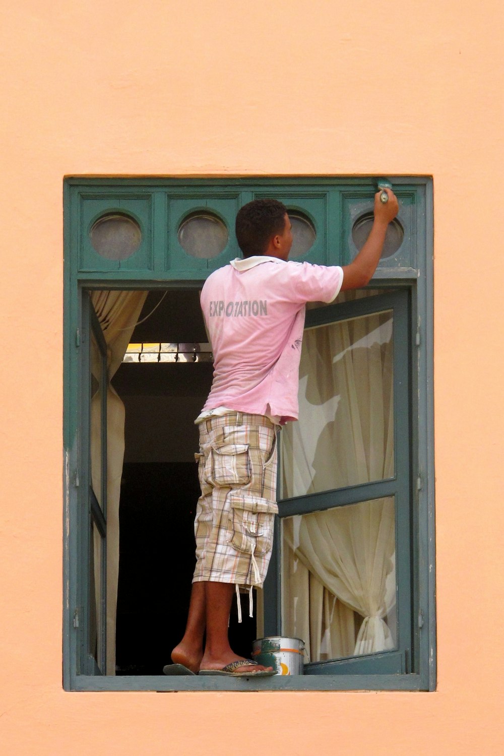 Hombre con camisa rosa y falda marrón a cuadros de pie frente a la puerta de madera marrón