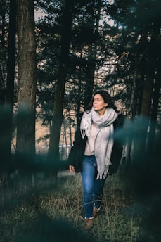 A woman in a cozy sweater and scarf walking through a leafy park in autumn