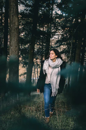 A stylish woman wearing a cozy sweater and jeans, walking in a city park during autumn.