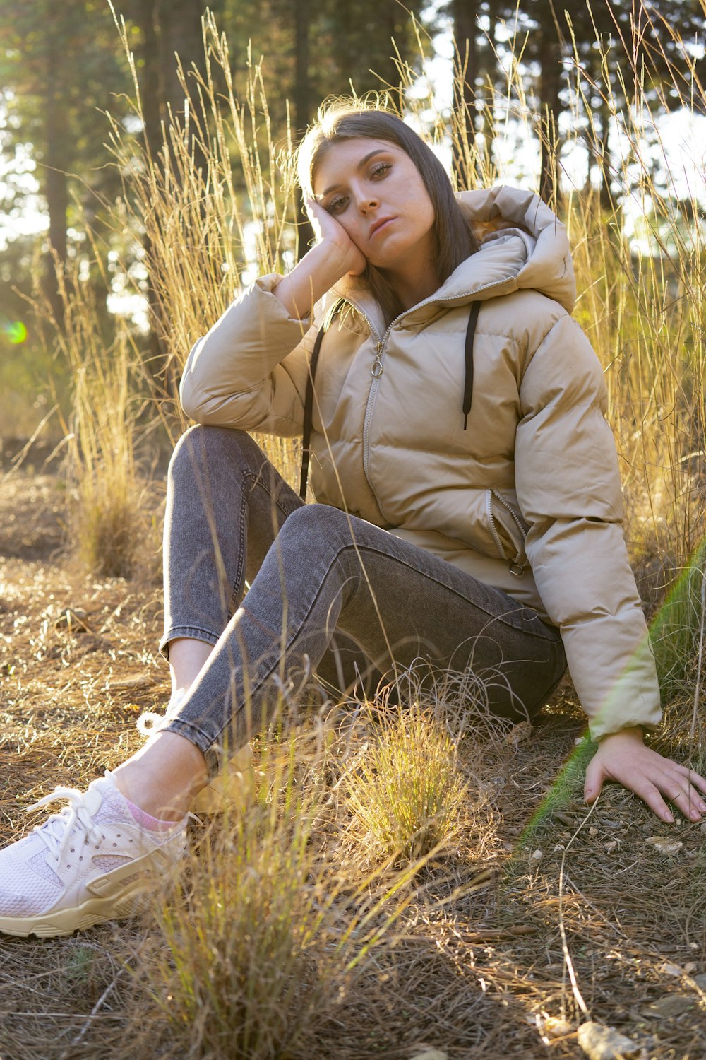woman in brown jacket and blue denim jeans sitting on brown grass during daytime