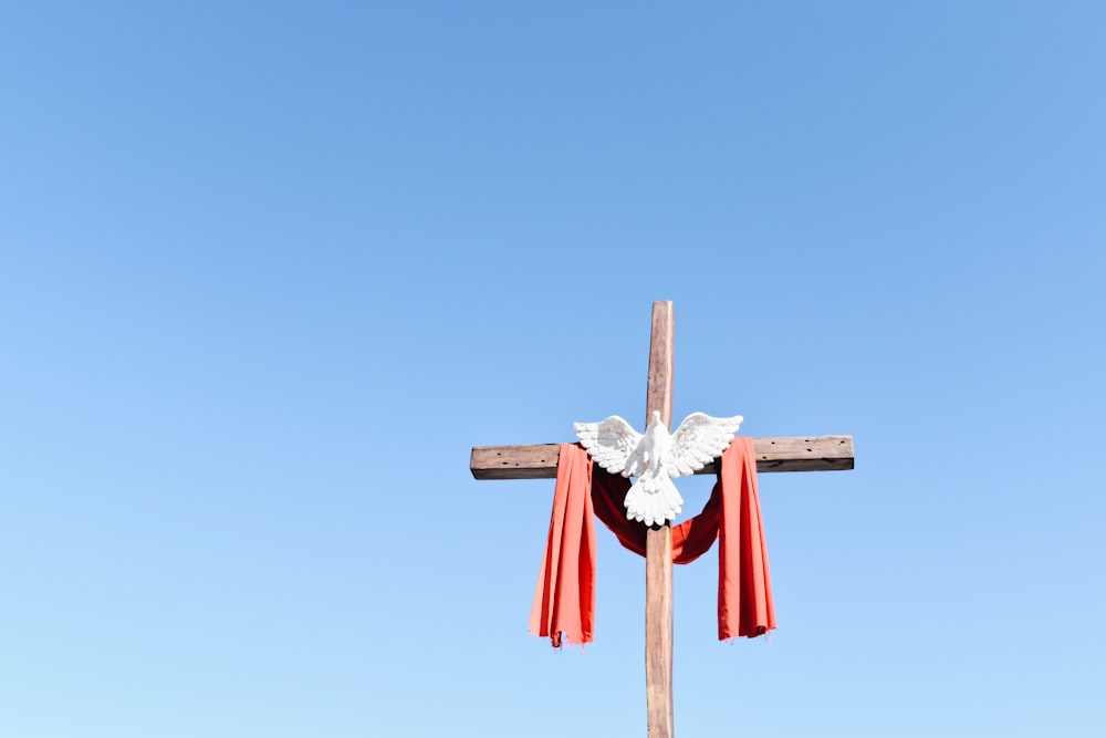 cruz de madeira marrom com fita vermelha e branca