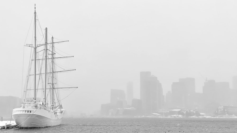 foto em escala de cinza do veleiro no mar perto de edifícios da cidade