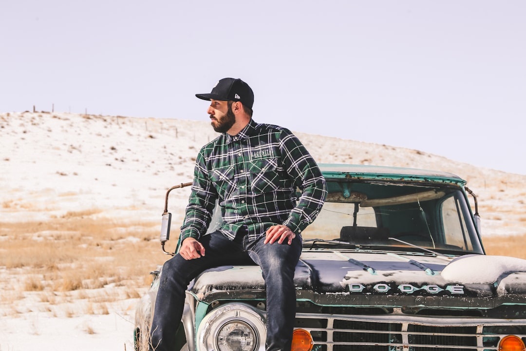 man in green and white plaid dress shirt and black cowboy hat sitting on black car