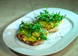 Top-down view of a creamy avocado toast topped with radishes and microgreens on a simple white plate.