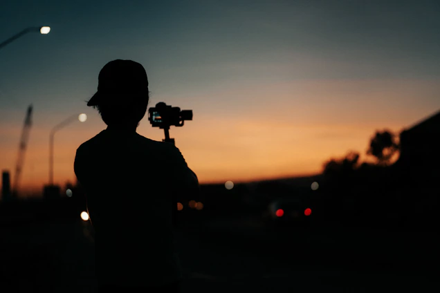 A candid shot of a videographer capturing a vibrant outdoor community event at sunset.