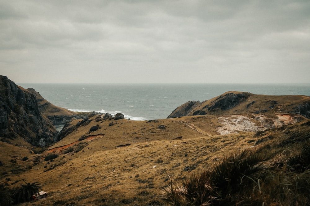 brown and green mountain beside sea under white clouds during daytime