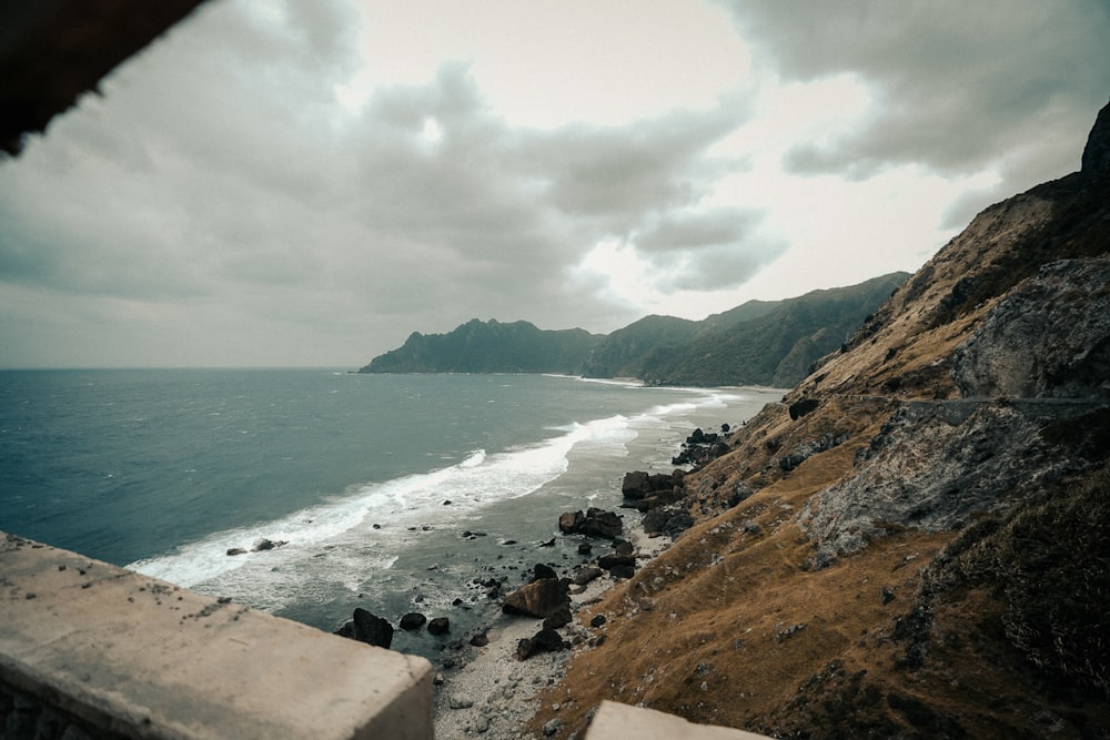 brown rocky shore near body of water under cloudy sky during daytime