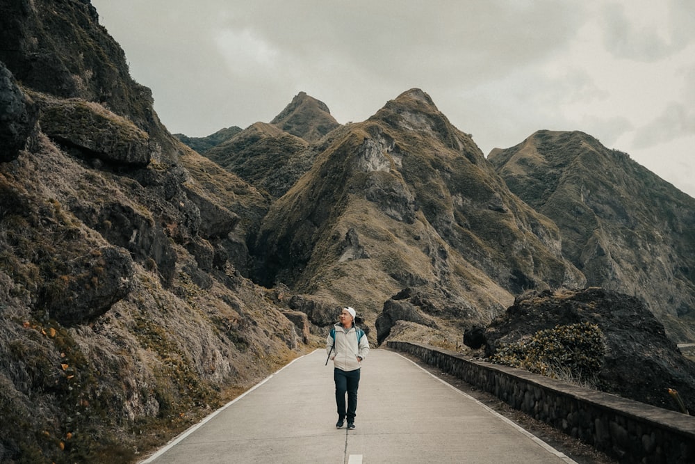 woman in white jacket and black pants walking on gray concrete pathway near brown mountain during